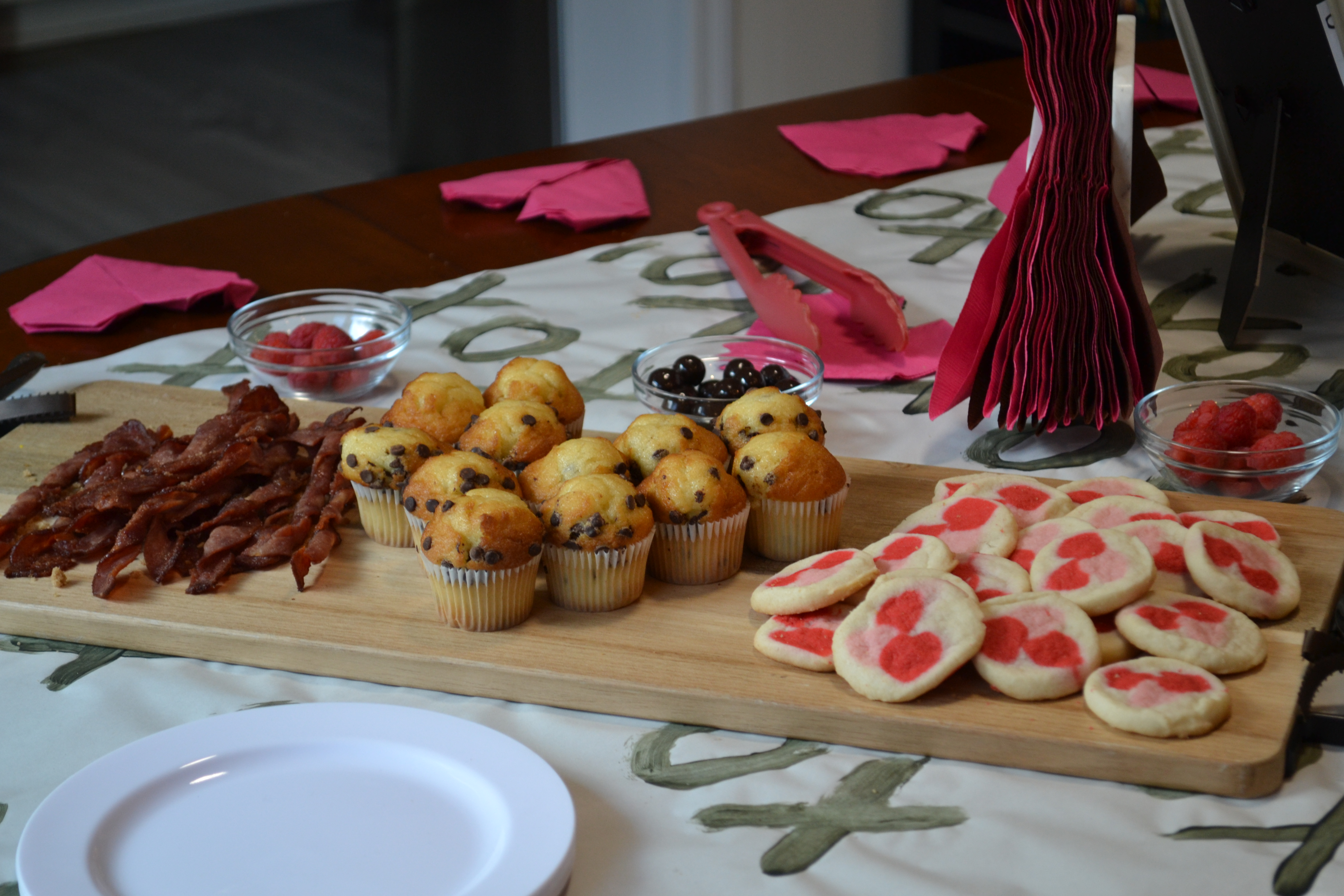 valentine's day brunch table of bacon, muffins, and cookies