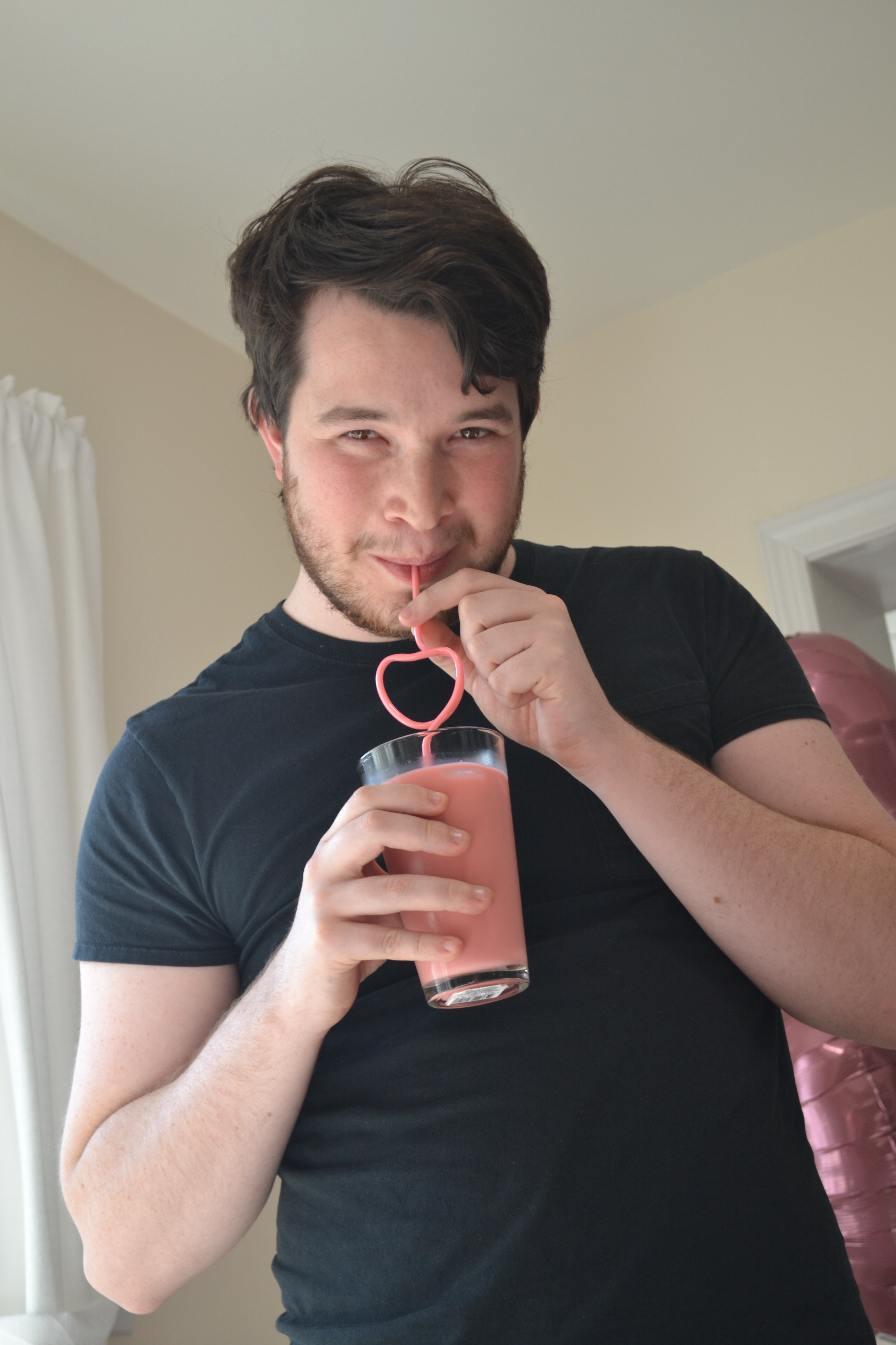 Photo of Russell Fleming drinking a pink coffee with a pink heart curly straw.