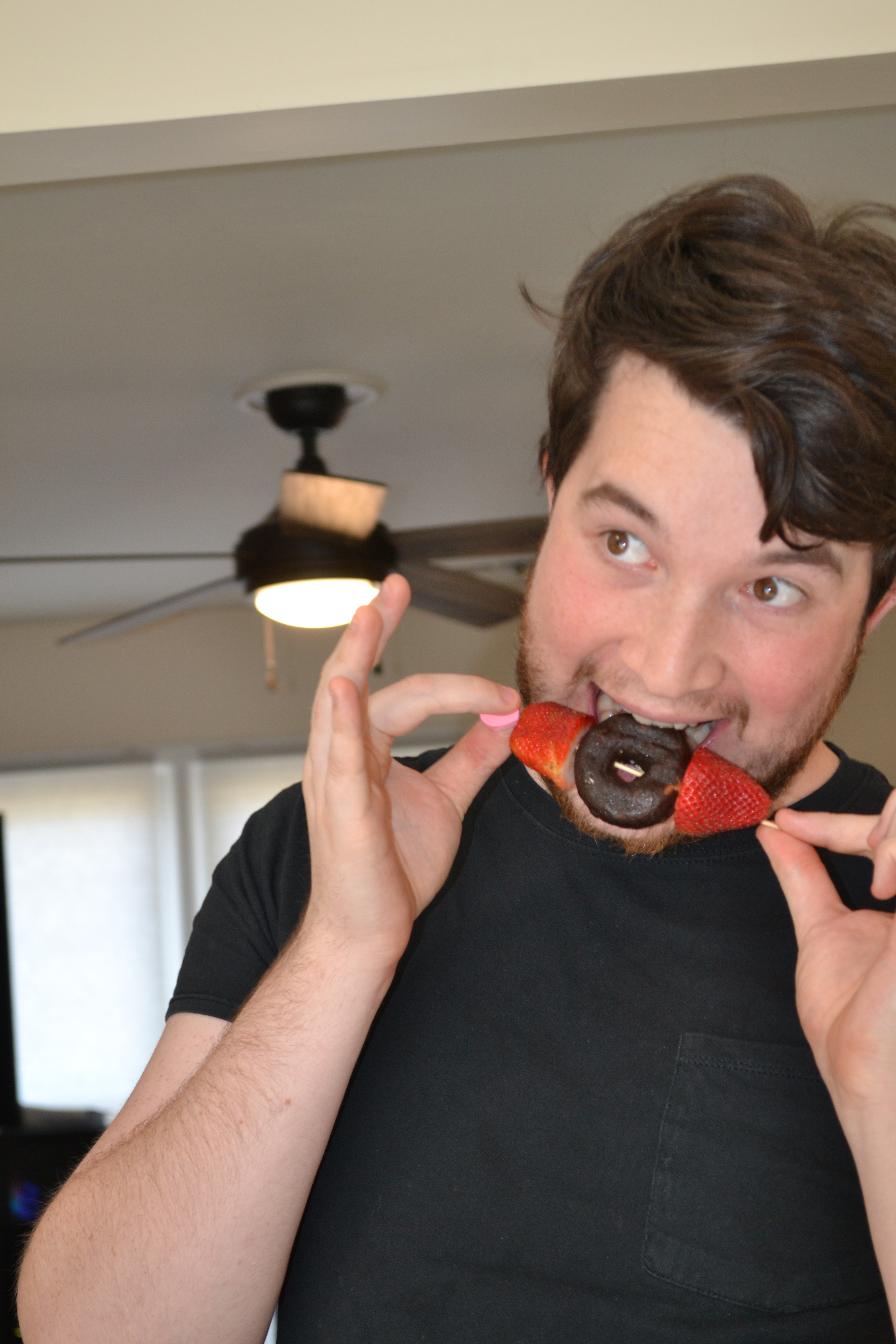 Photo of Russell Fleming biting a skewer of a donut and strawberries.
